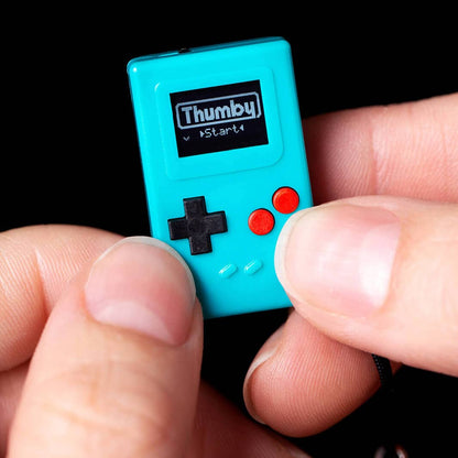 Small teal game with 'Thumby' branding held between fingers against a black background