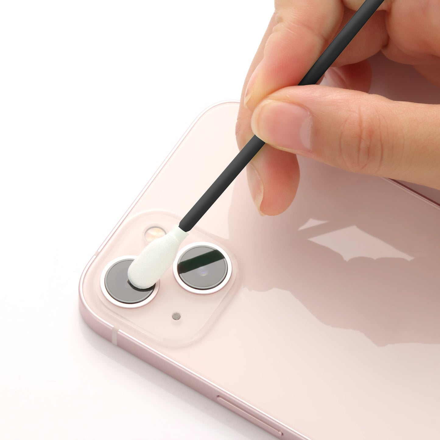 Person cleaning a smartphone camera lens with a white swab on a white background