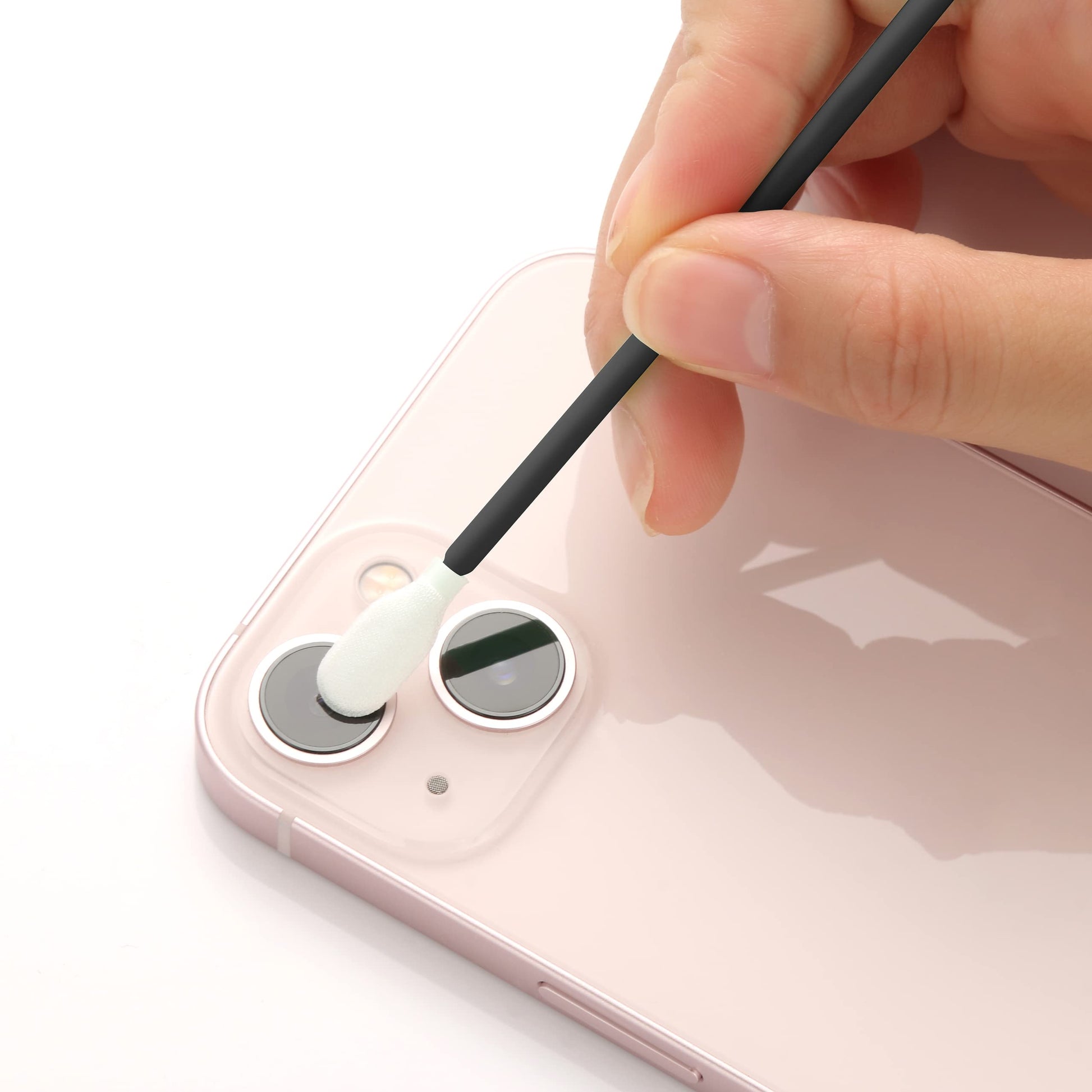 Person cleaning a smartphone camera lens with a white swab on a white background
