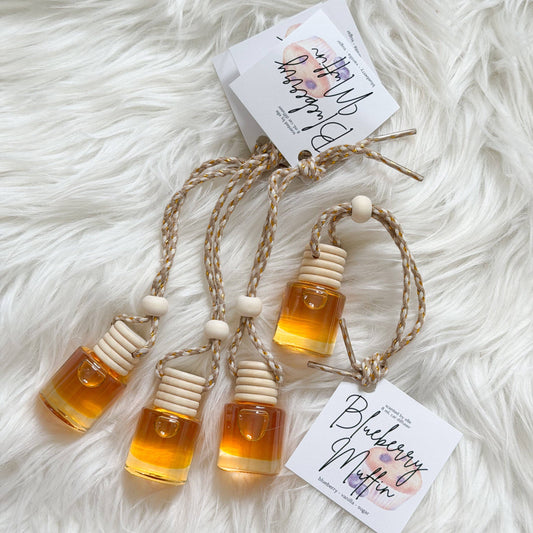 Four amber glass bottle-shaped ornaments with white wooden cap details and jute cords, displayed on a white faux fur background with two paper tags reading Blueberry Muffin.