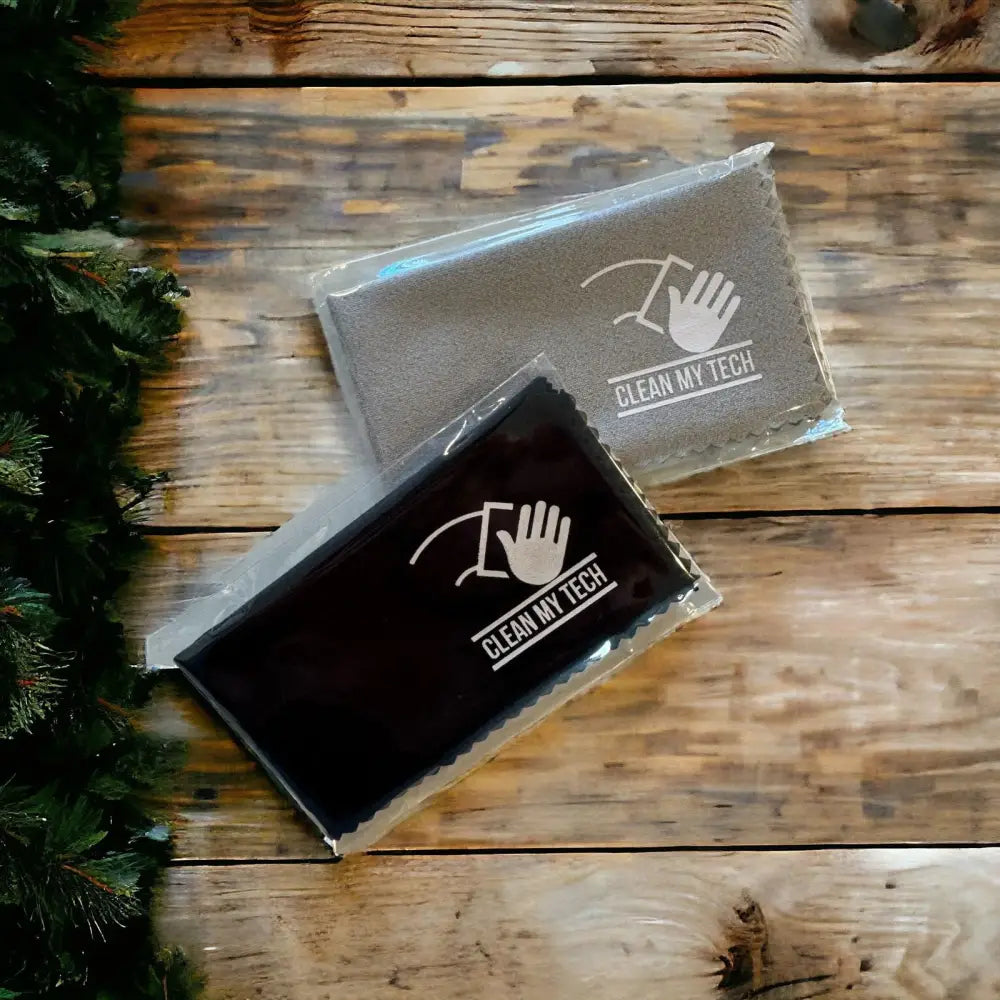 Two ’clean my tech’ microfiber cleaning cloths, one gray and one black, each packaged in clear plastic with a white logo featuring a hand wiping a screen.