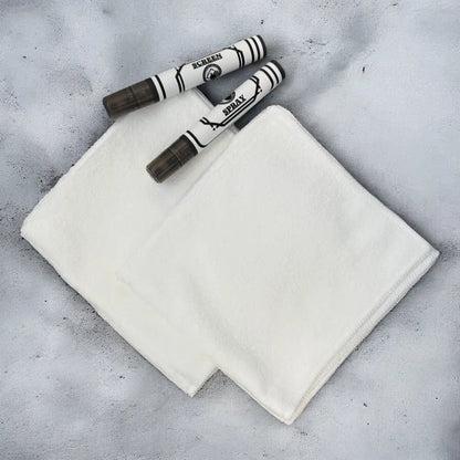 White microfiber cleaning cloth with two black-and-white spray bottles resting on top