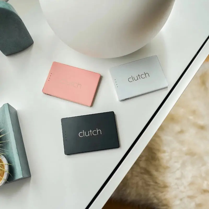 Three rectangular clutch portable chargers in pink, silver, and black.
