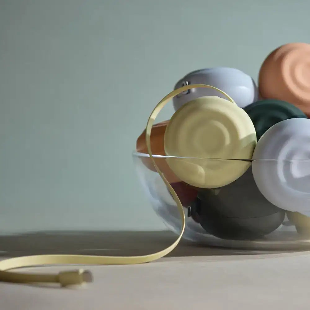 A sleek, gold-colored usb cable with a minimalist design lies coiled beside a clear glass bowl filled with colorful, matte-finished spherical objects.