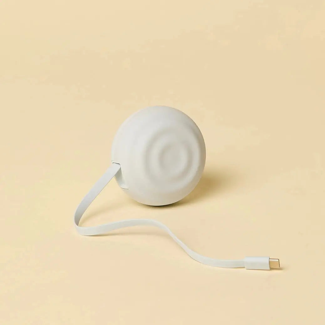 White spherical portable charger with a smooth matte finish and an integrated usb-c cable extending from its side.