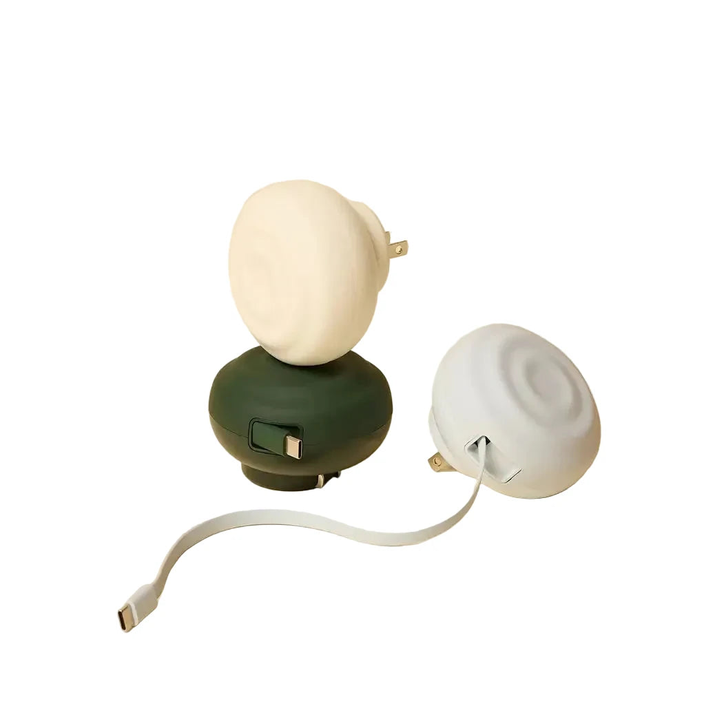 Two compact, round portable chargers with a matte finish—one in dark green and one in off-white—each featuring an integrated plug and usb-c cable.