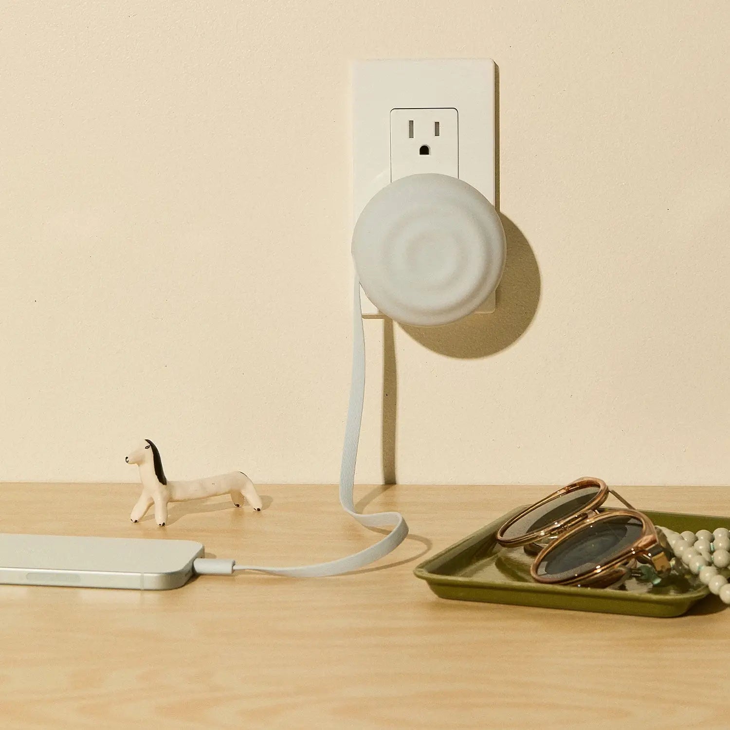 White circular smart plug with a soft, matte finish and an integrated charging cable.