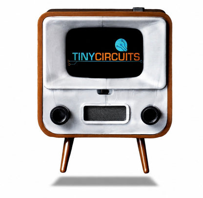 A retro-style miniature television set with a brown wood-grain frame, white faceplate, and two small legs, shown on a white background with a shadow underneath. The screen displays the brand logo 'TINYCIRCUITS'.