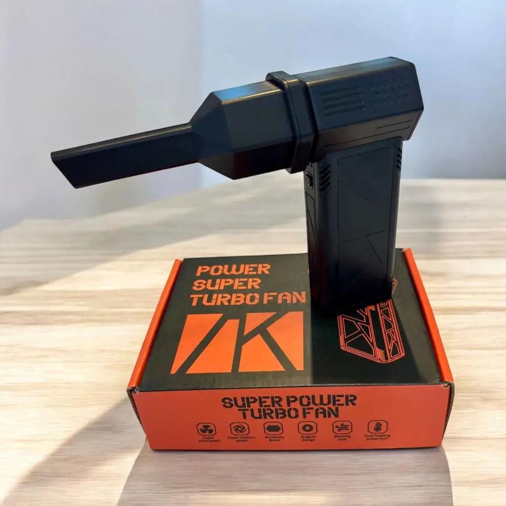 Black plastic handheld super turbo fan with a sleek, angular design and an orange branded box underneath.