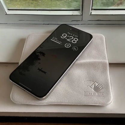 Silver-framed iphone 13 pro max resting on a soft, off-white microfiber cleaning cloth with an embroidered ’clean my tech’ logo.