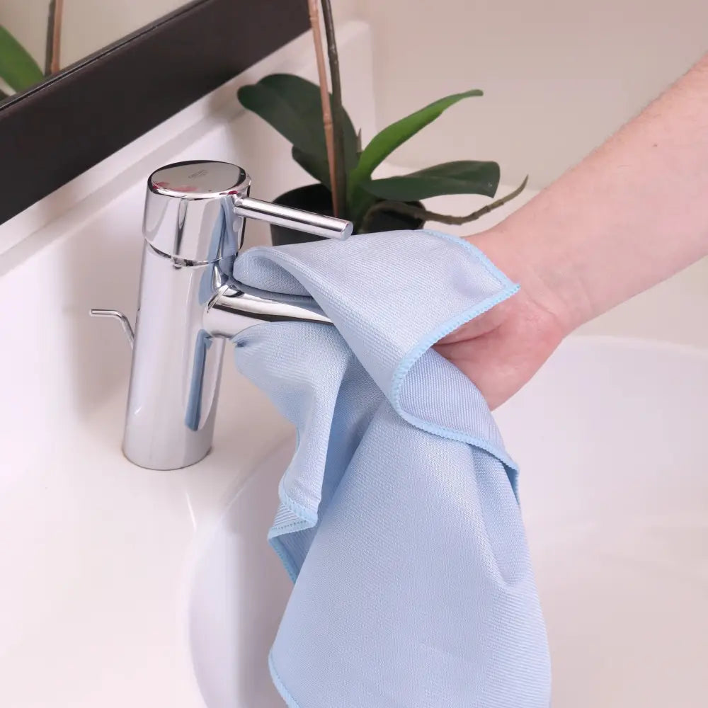 Light blue microfiber cloth being used to wipe a chrome faucet.