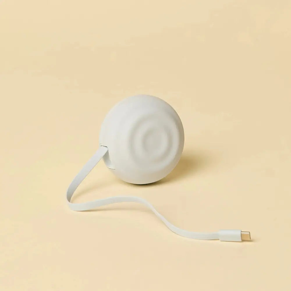 White spherical portable charger with a smooth matte finish and an integrated usb-c cable extending from its side.