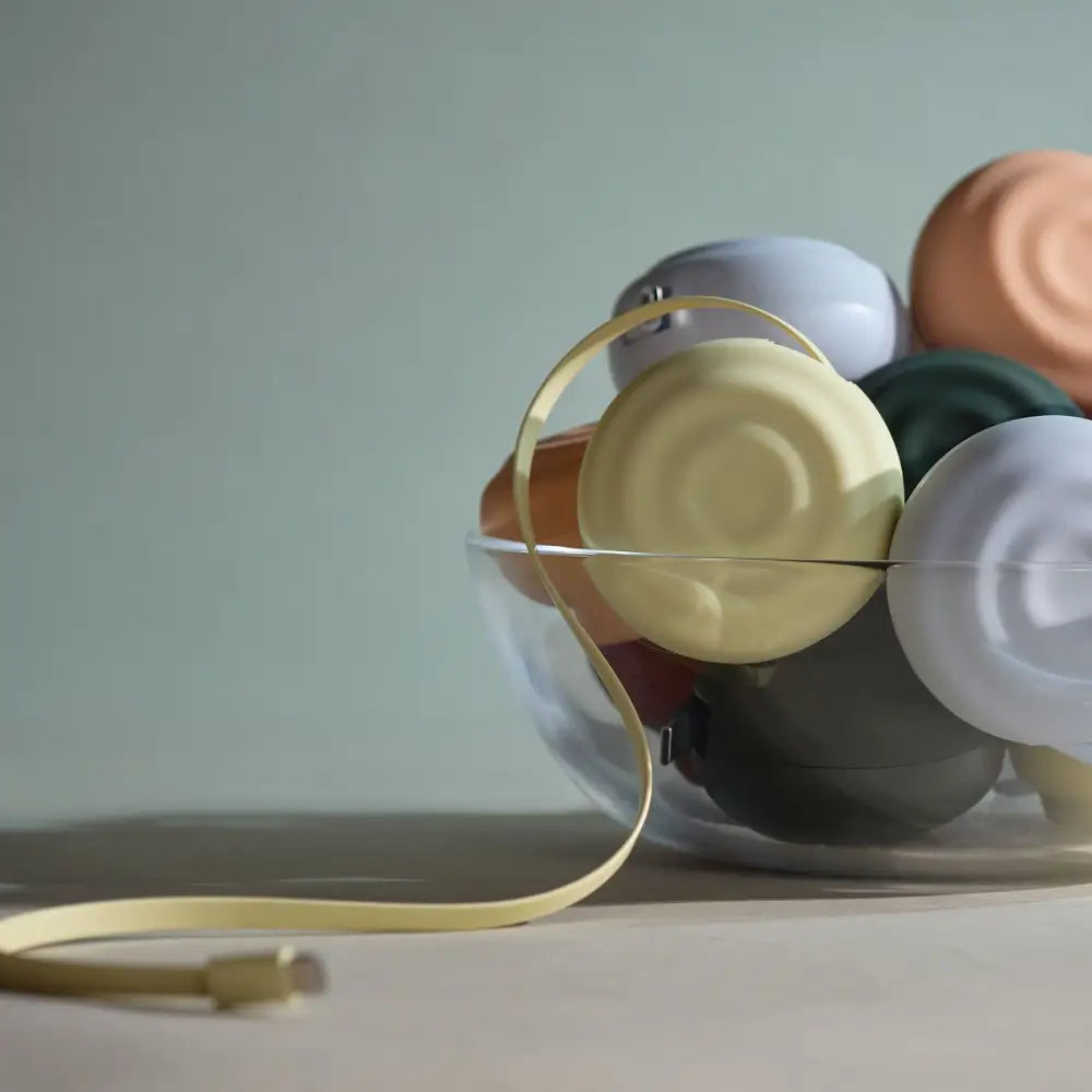 A sleek, gold-colored usb cable with a minimalist design lies coiled beside a clear glass bowl filled with colorful, matte-finished spherical objects.