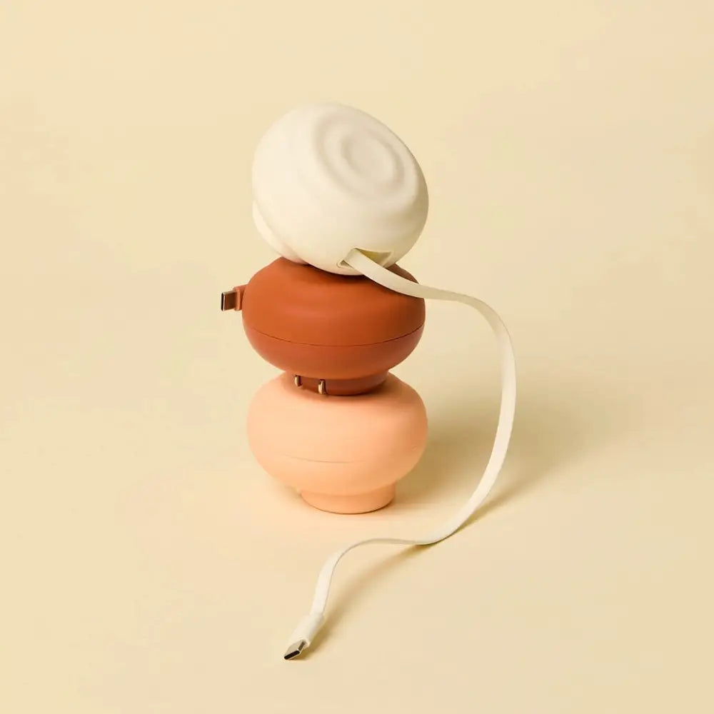 A sleek, three-tiered portable charger with a matte terracotta base and white top tier, featuring soft rounded contours.