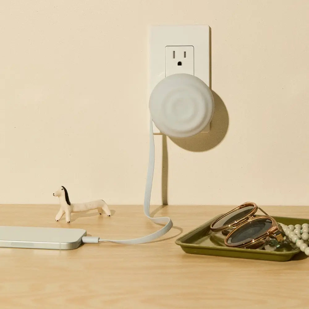 White circular smart plug with a soft, matte finish and an integrated charging cable.