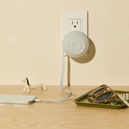 White circular smart plug with a soft, matte finish and an integrated charging cable.