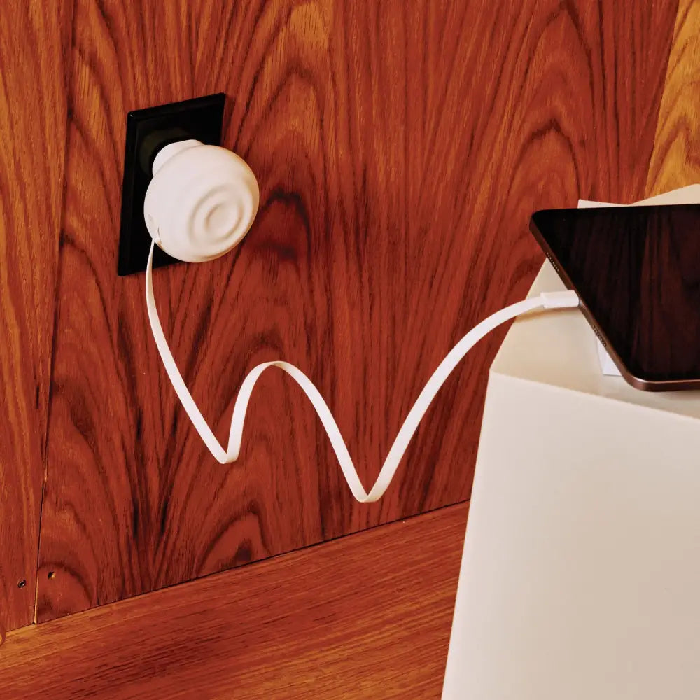White, round charging station with a coiled cable plugged into a wall outlet.