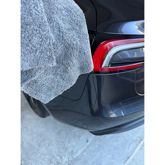 A plush, medium-gray towel with a soft, textured surface draped over the rear side of a sleek black tesla model s.
