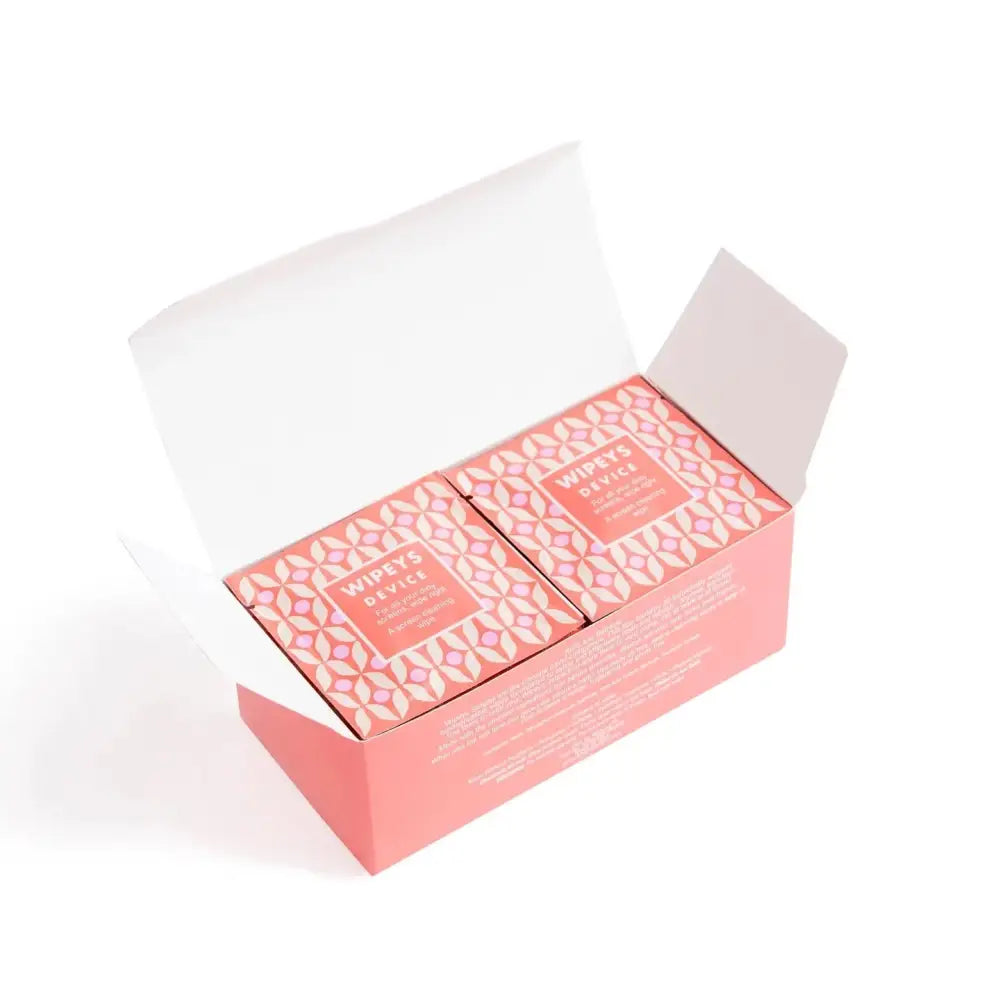 Pink rectangular box with white and light pink geometric pattern, containing two smaller boxes labeled ’wipes’ device’ for facial cleansing.